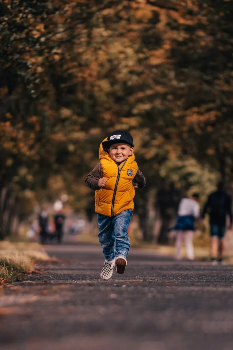 A child in a bright jacket running down a tree-lined path