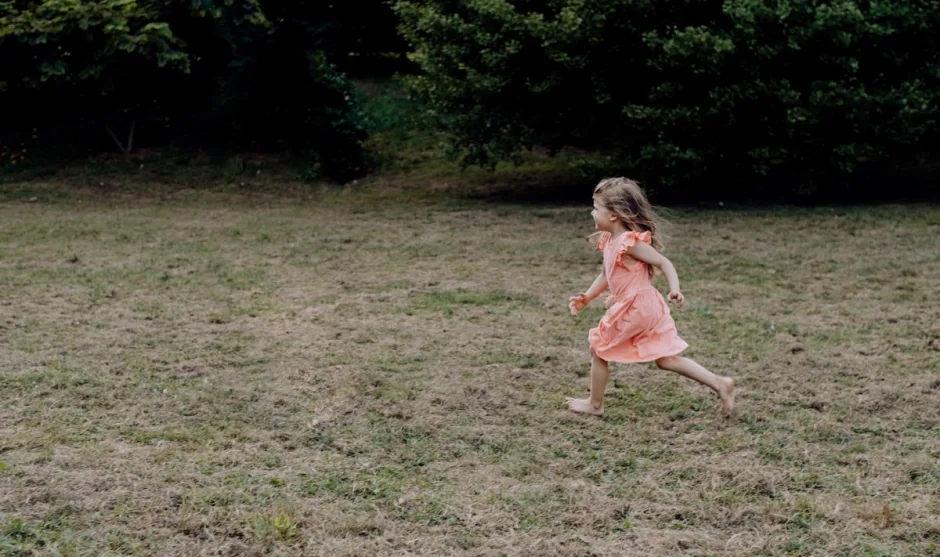 A girl in a pink dress running across a green field