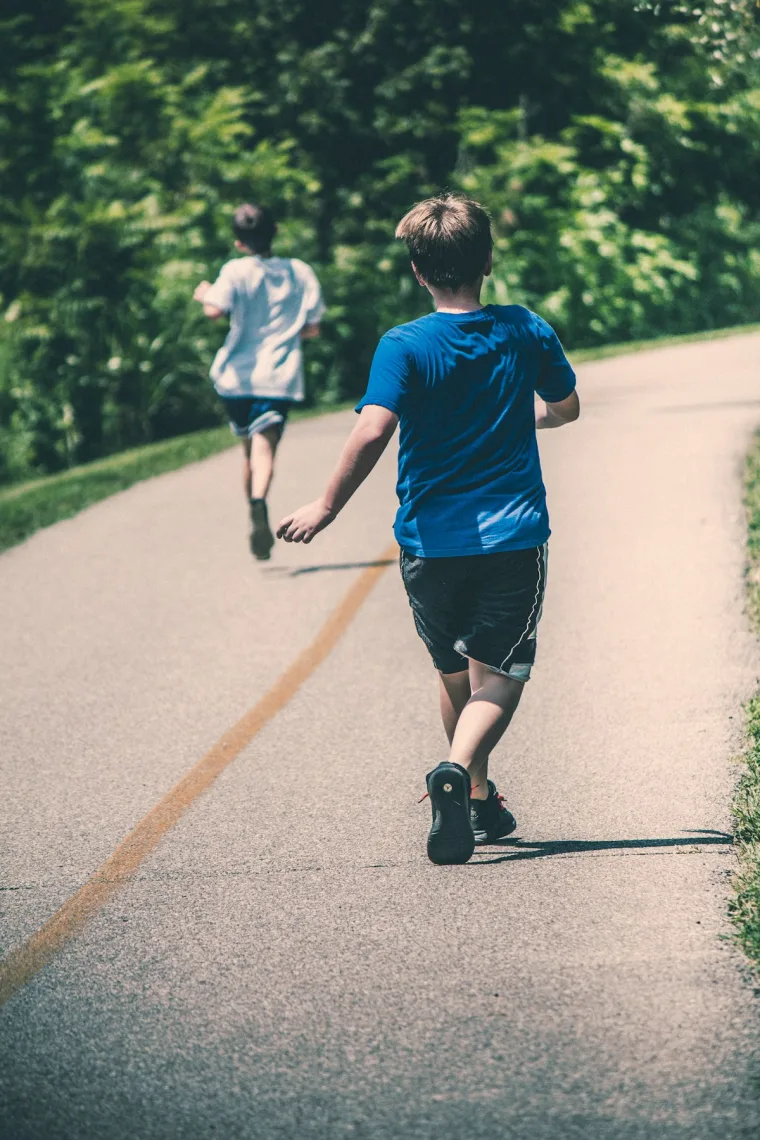Two kids running down an open road on a summer day